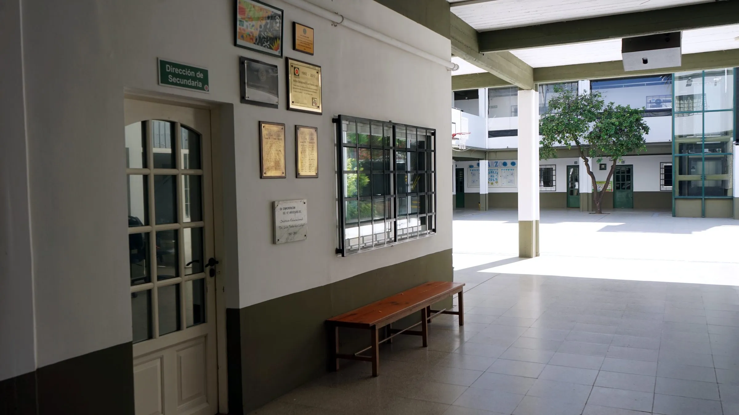 Galería de acceso a Dirección, con las placas institucionales y el patio al fondo